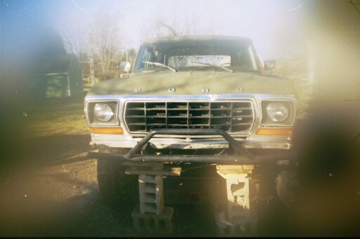 Front view of a green Ford Bronco on blocks, with a custom bumper