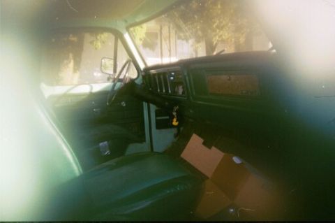 1979 Ford Bronco - The interior of a green vehicle, showing the dashboard, steering wheel, and seats. Boxes are visible on the floor.