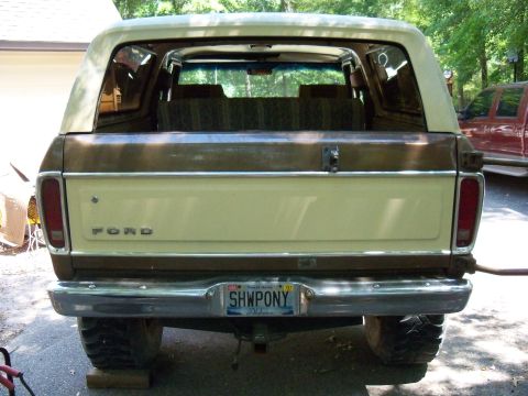 1979 Ford Bronco - The rear of a Ford Bronco, showing its two-tone paint and license plate. A red truck is parked nearby.