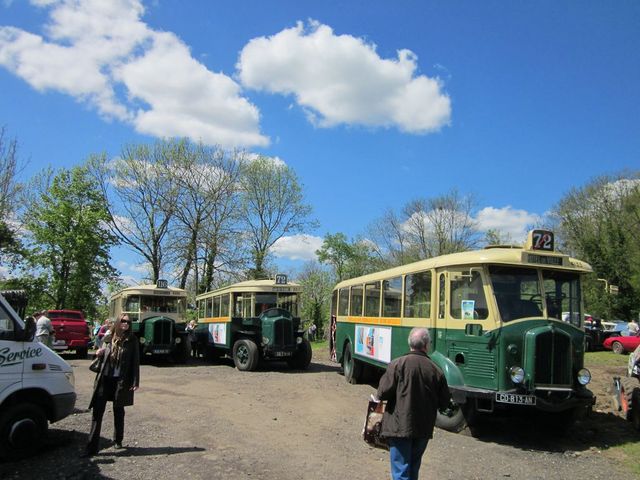 Several old buses parked outside, one with a '72' sign on top. A white van is on the left