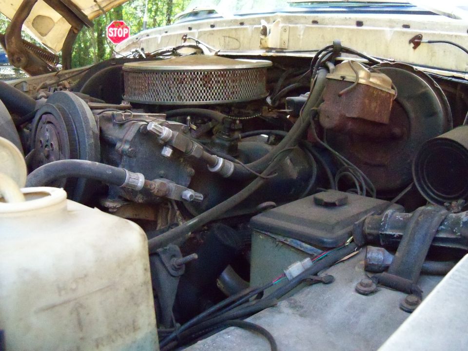 Engine bay with air cleaner, hoses, and brake fluid reservoir visible. A stop sign is in the background