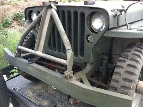 1986 Ford Bronco - Front view of an olive drab jeep, a prominent brush guard and tires.