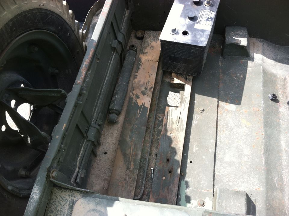 Close-up of a vehicle's frame with a battery on top. Shows a tire and suspension components