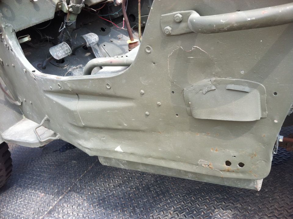 Olive drab Jeep interior showing pedals, floor pan, and dented side panel with rivets