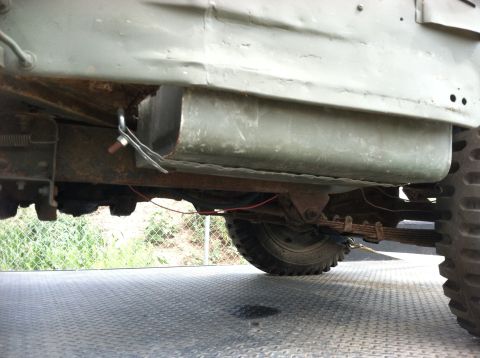 1986 Ford Bronco - The undercarriage of a green military-style vehicle is visible, its fuel tank and leaf spring suspension system.