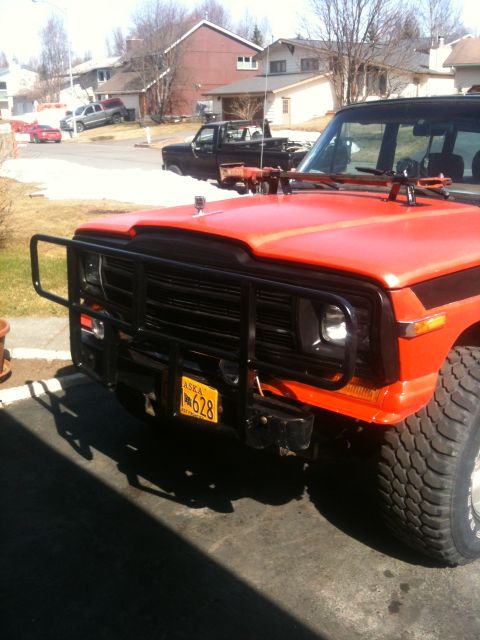 1990 Chevrolet Suburban - This red SUV features a prominent brush guard and a gun rack mounted on the hood. An Alaska license plate is visible on the front.