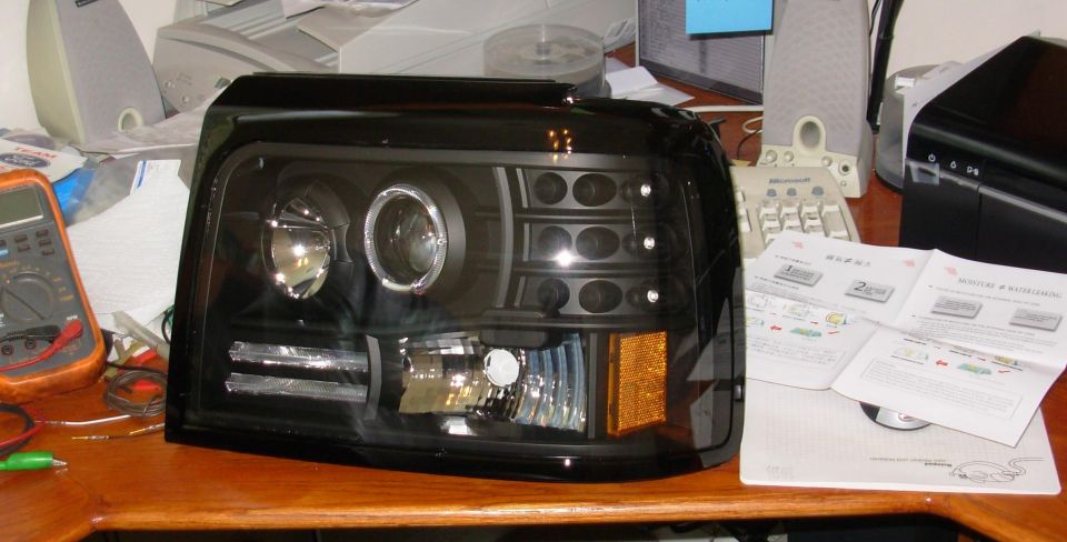 Black projector halo headlight assembly with amber turn signal on a desk