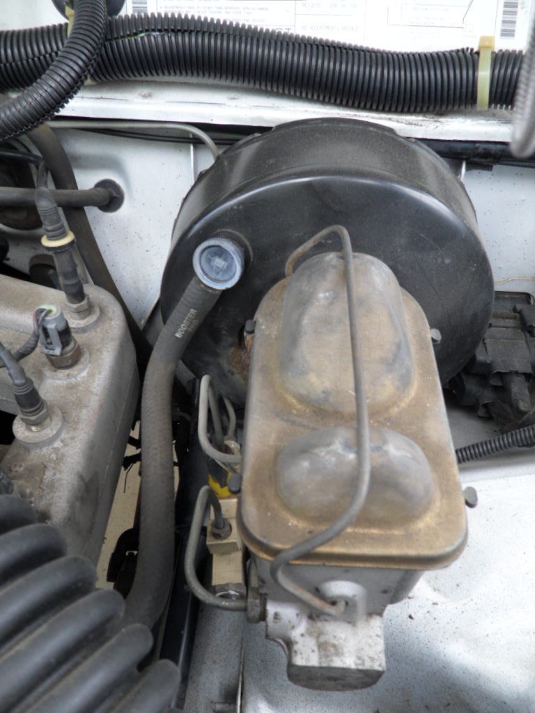 Brake booster and master cylinder assembly in engine bay. Black ribbed hose connects to booster