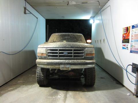 1992 Ford Bronco - A dirt-covered 1992 Ford Bronco is parked head-on inside a car wash bay.