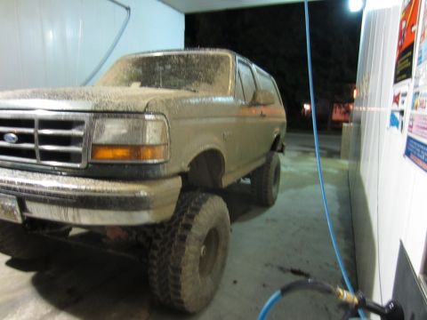 1992 Ford Bronco - This mud-covered 1992 Ford Bronco is parked in a wash bay, likely after an off-road excursion.
