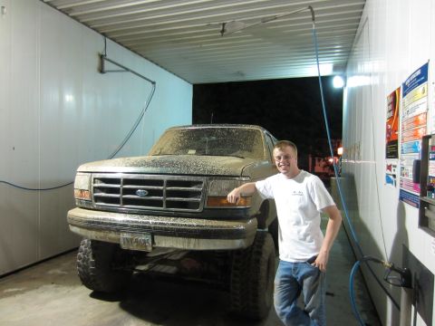 1992 Ford Bronco - A man poses with a mud-covered 1992 Ford Bronco at a self-service car wash.