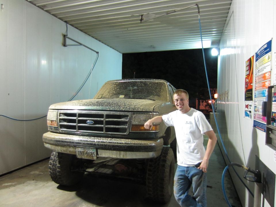 Mud-covered 1992 Ford Bronco 3q-front view with man leaning on it