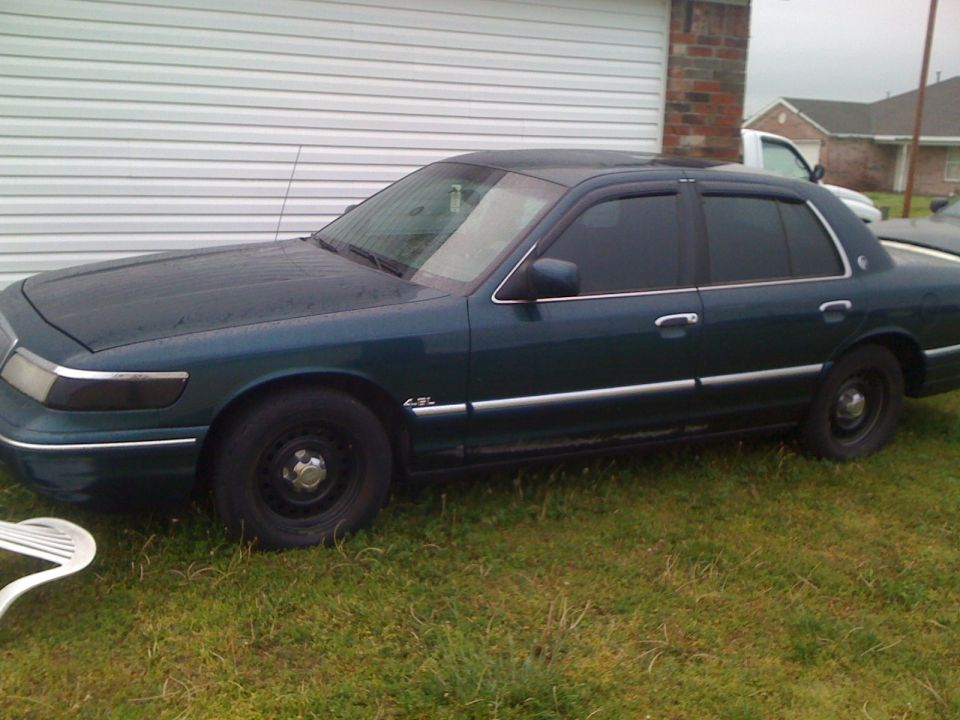 Dark green Mercury Grand Marquis sedan with black steel wheels parked on grass beside a garage