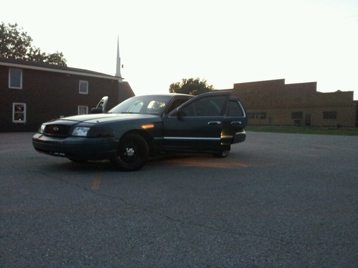 Dark sedan with front and rear doors open, parked in a lot near buildings