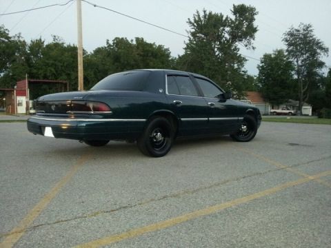1994 Mercury Grand Marquis - A dark green sedan with black steel wheels is parked in a lot under an overcast sky.