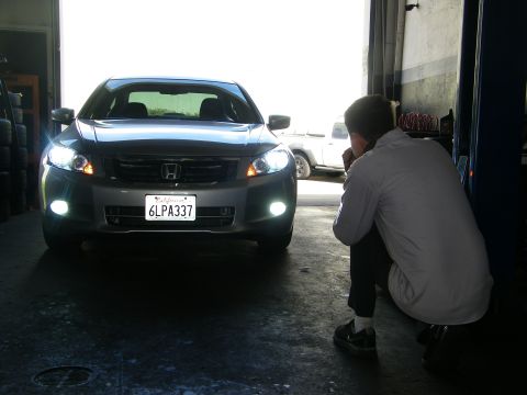 2010 Honda Accord - A person kneels in front of a Honda Accord inside a garage, observing its illuminated headlights and fog lights.