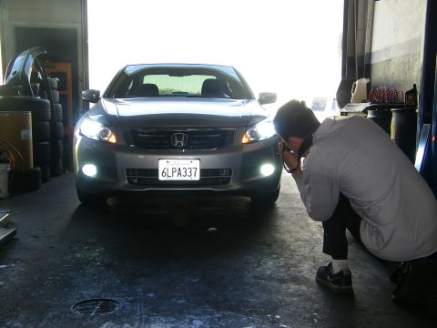 2010 Honda Accord - A photographer crouches to take a picture of a silver sedan's front end in a garage setting.