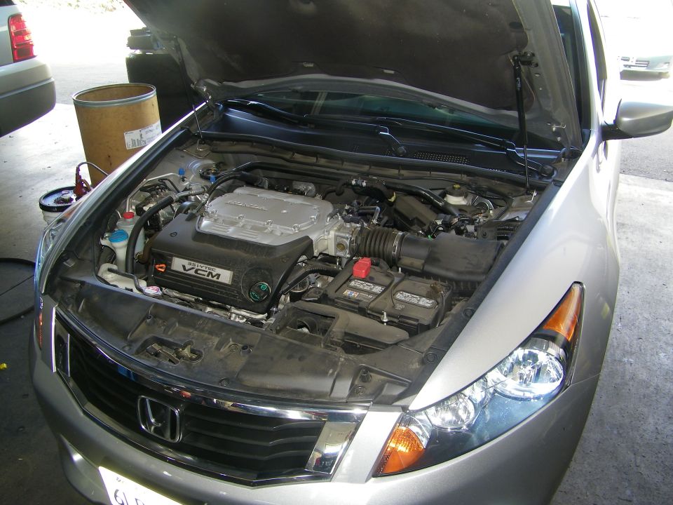 Engine bay of a silver Honda Accord, hood open. VCM badge visible on engine cover