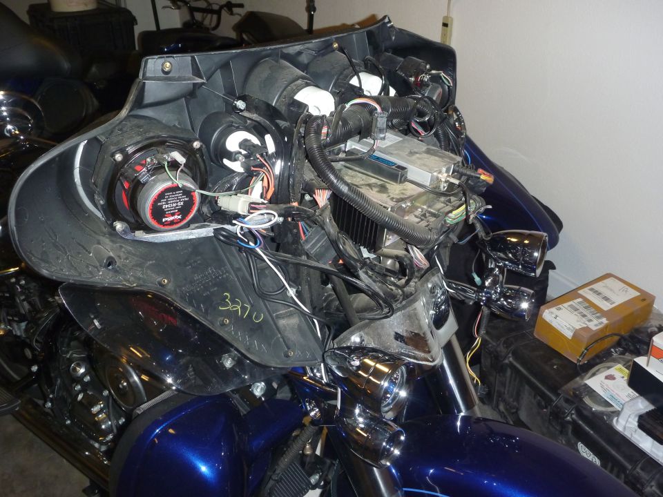 Dark blue Harley touring bike with fairing off, exposing wiring, speaker, and electronics in a garage