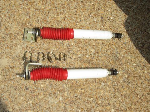 1992 Ford Bronco - Two shock absorbers and their associated U-bolts and nuts are displayed on a textured ground.