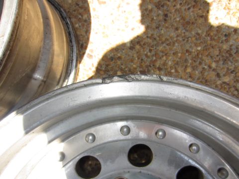 1992 Ford Bronco - Close-up of a damaged aluminum wheel rim, showing dents and scratches on the lip. Another wheel is visible in the background.