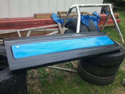 1979 Ford Bronco - A black door panel with a bright blue insert is shown, resting on a stack of tires with a roll bar in the background.