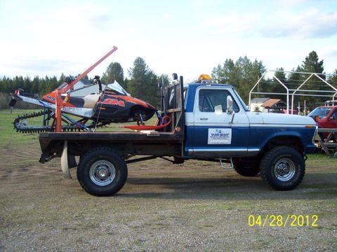 2004 Arctic Cat King Cat 900 - A flatbed truck carries a snowmobile, secured with straps and a small crane, on its cargo bed.