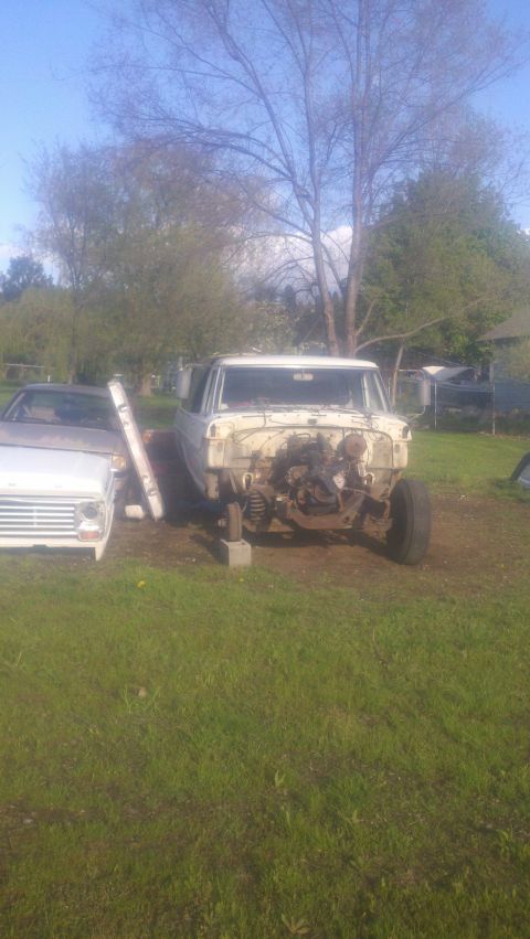 1988 Ford Bronco - A white Ford truck, missing its engine, sits on grass beside another vehicle under a clear sky.