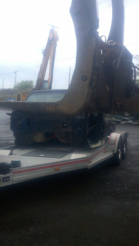 1988 Ford Bronco - A severely damaged vehicle body is being lifted by a large claw, resting on a trailer.