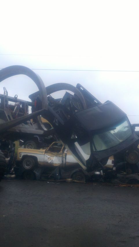 1988 Ford Bronco - A scene of multiple crushed vehicles in a junkyard, with a white and yellow truck partially visible beneath other wreckage.