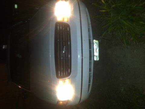 2000 Ford Crown Victoria - The front of a white 2000 Ford Crown Victoria is visible at night, illuminated by its headlights.