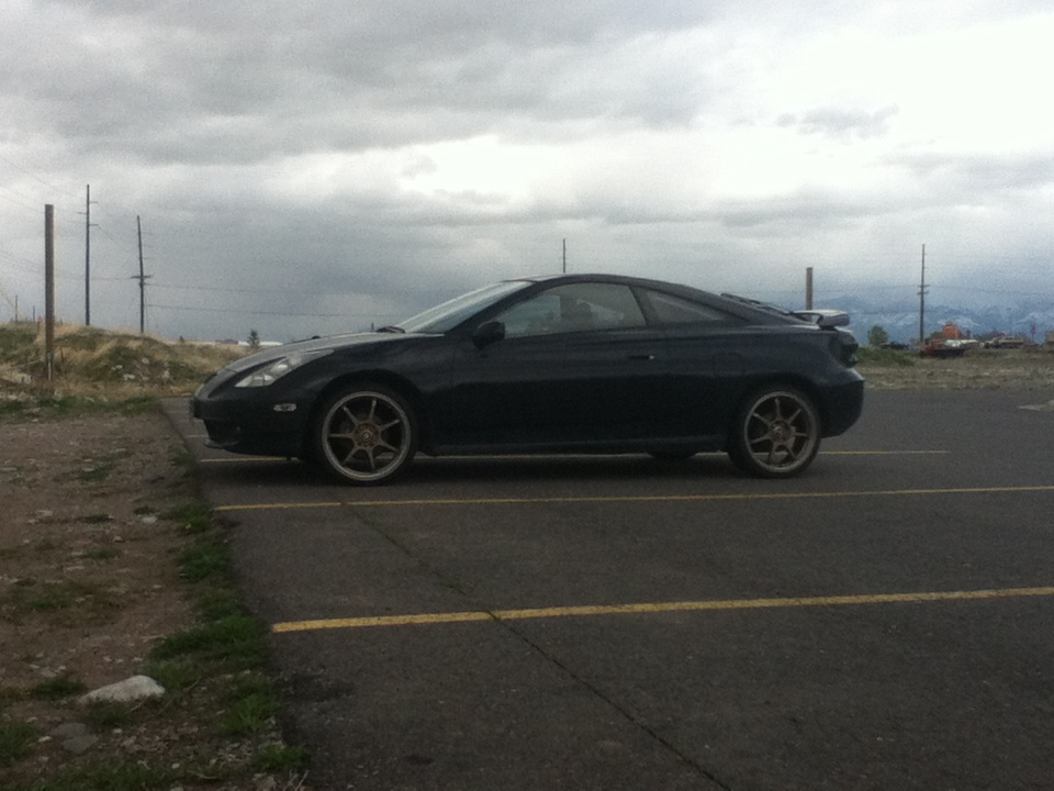 Black coupe parked on asphalt with a cloudy sky