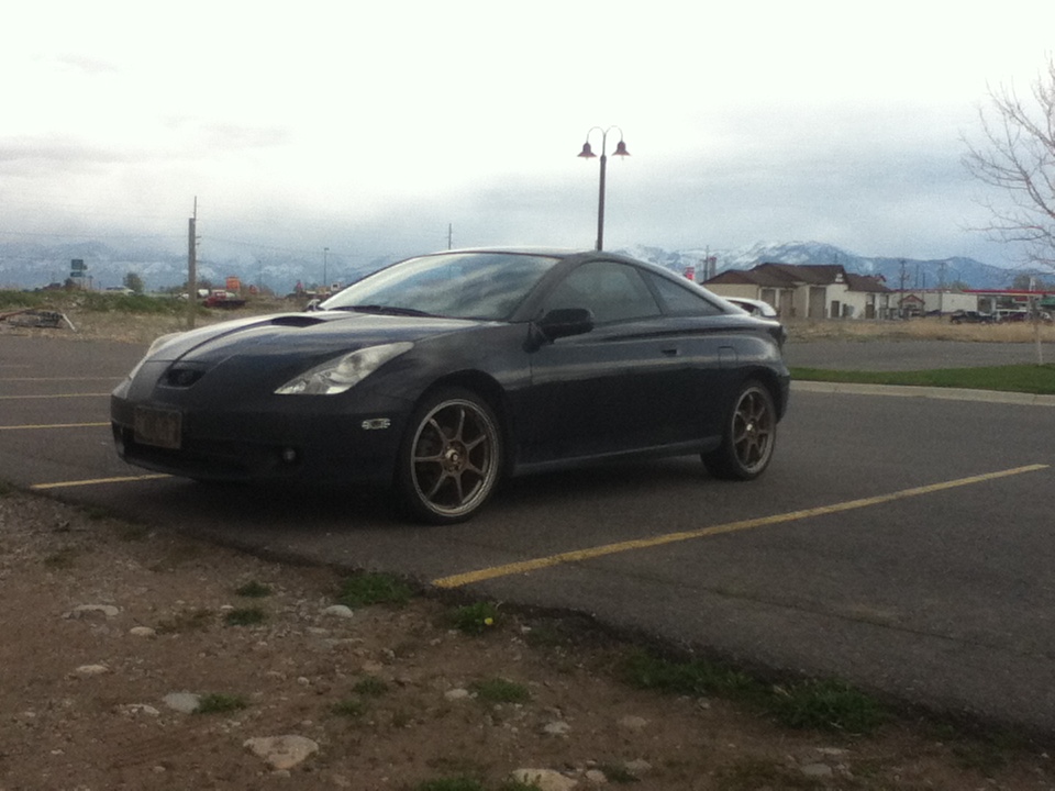 Black coupe parked in a lot, front 3/4 view. Aftermarket wheels and a hood scoop are visible
