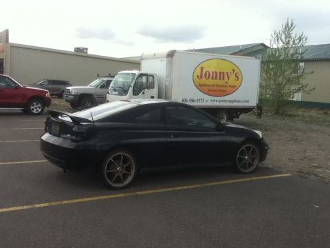 2006 Ford E350 - A black coupe with a spoiler is parked in a lot next to a white delivery truck with 'Jonny's' logo.