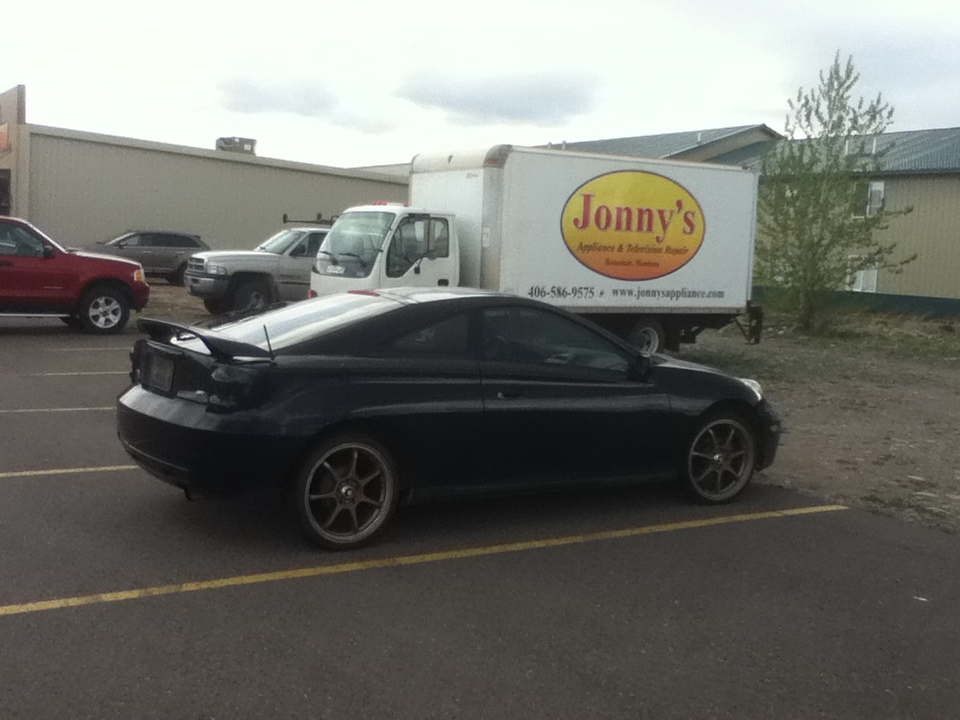 Black coupe with spoiler parked next to a delivery truck