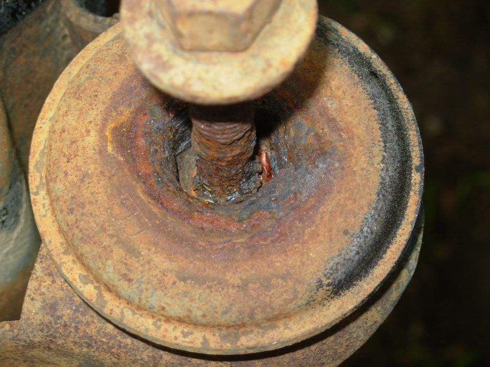 Rusted body mount bolt, washer and corroded mount cup with tar residue