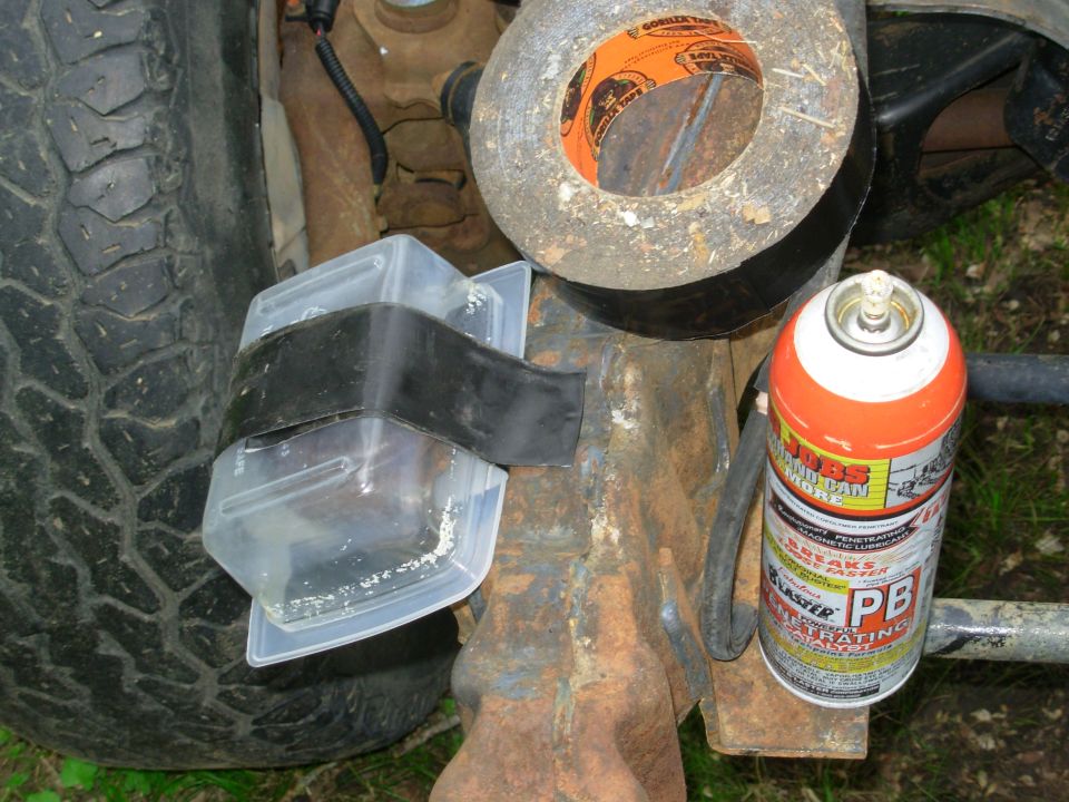 Truck body mount repair with PB Blaster can, taped bushing and drip container near rusty frame
