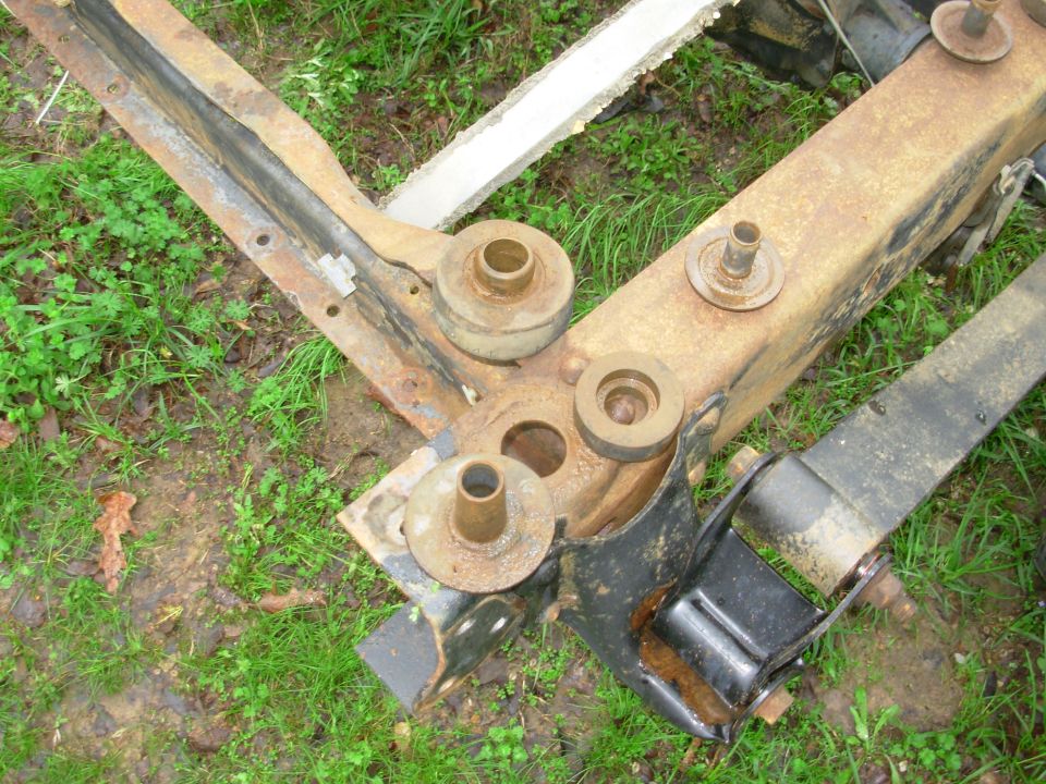 Rusty truck frame with body mount bushings and studs lying on grass