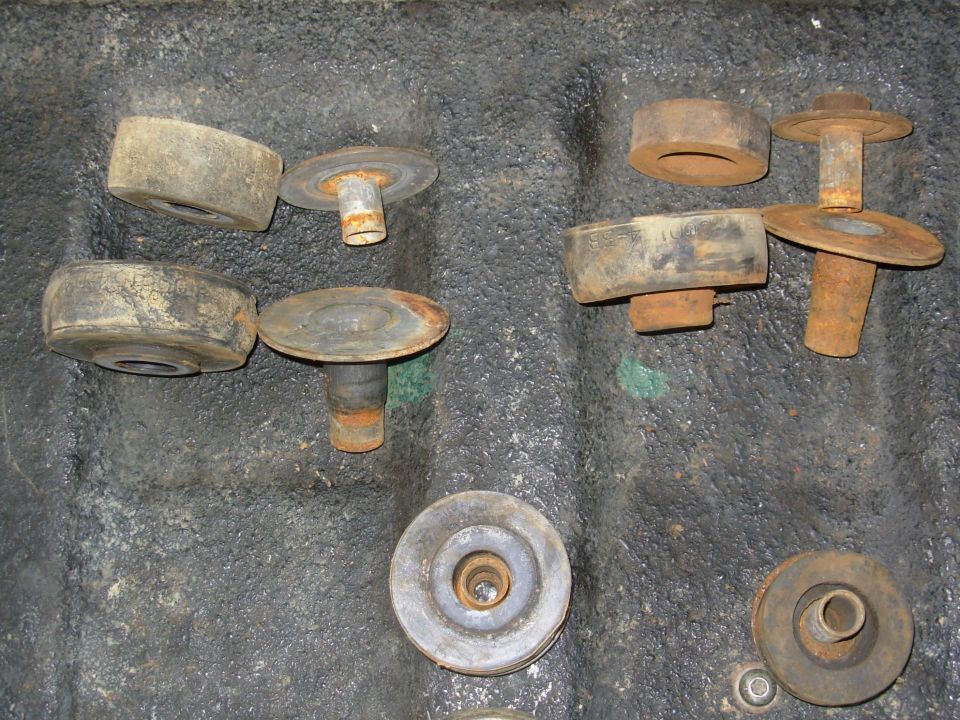 Rusty rubber body mount bushings and metal brackets laid out on dirty concrete