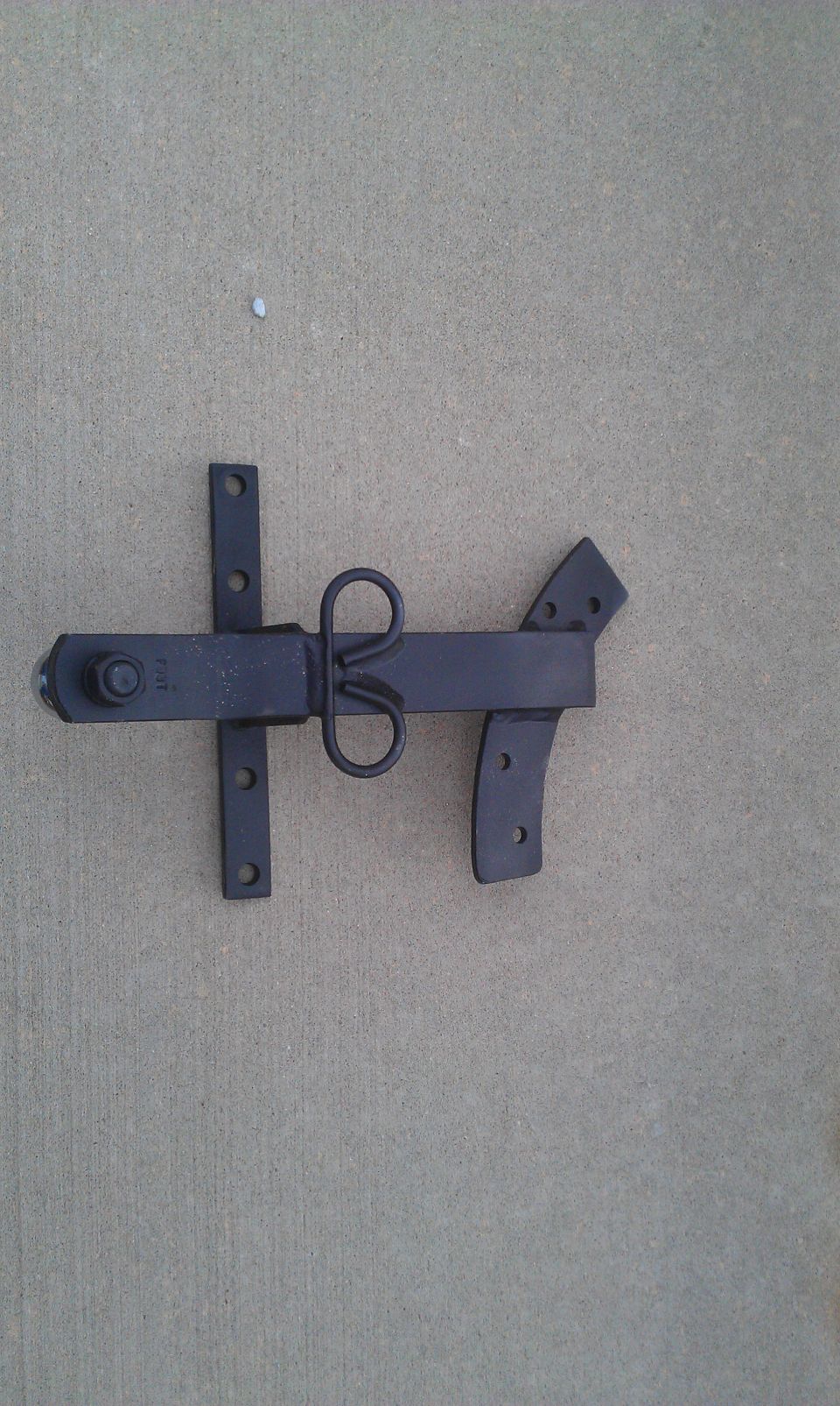 Black metal gate latch with a looped handle, mounted on concrete