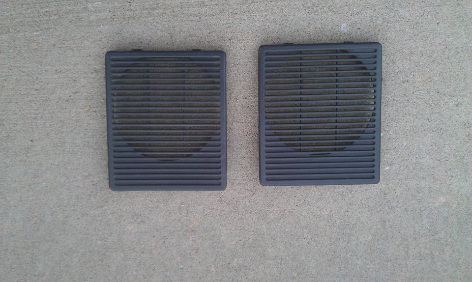 Two rectangular black speaker grilles with horizontal slats, lying on a concrete surface