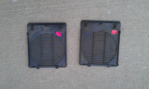 1991 Ford Festiva - Two black plastic speaker grilles are shown lying on a concrete surface.