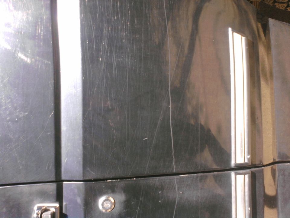 Close-up of scratched black vehicle panel with chrome trim strip and round key lock cylinder