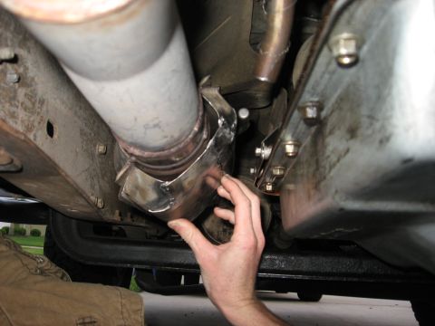 1994 Ford Bronco - A person is working on the exhaust system of a vehicle, holding a clamp in place.