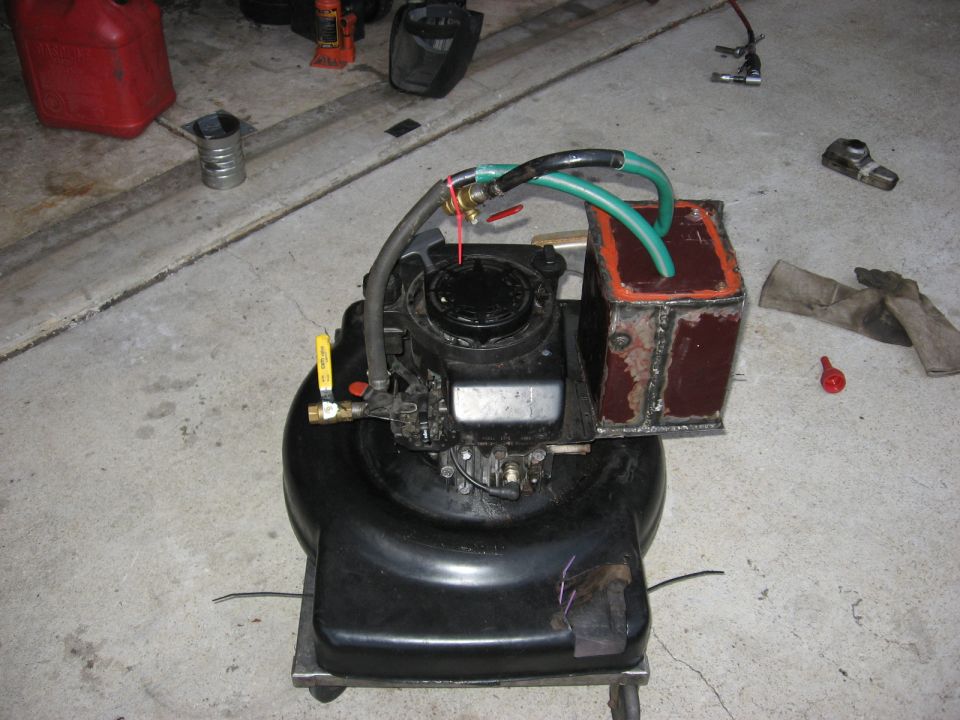 ATV fuel tank with carburetor, brass petcock and green fuel hoses on a garage floor