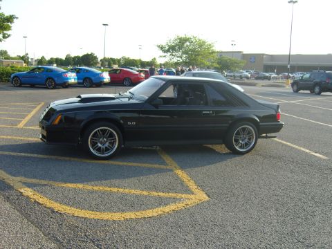 2007 Ford Mustang - A black Ford Mustang from the late 1980s is parked in a lot with other vehicles.