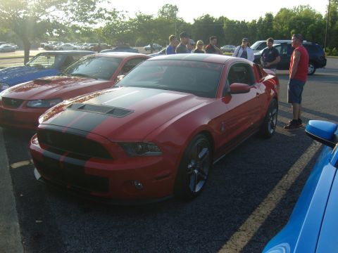 2007 Ford Mustang - A red 2007 Ford Mustang with black racing stripes is parked at a car meet.