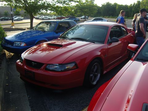 2007 Ford Mustang - Red Ford Mustang with a hood scoop parked in a lot with other vehicles.