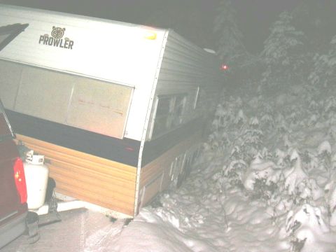 1991 Ford Bronco - A Prowler travel trailer is partially obscured by snow and trees in a wooded area at night.