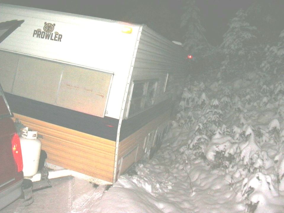 Travel trailer with 'Prowler' logo stuck in snowy woods at night